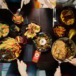 Ylhäältä kuvattu ravintolapöytä, jossa useita annoksia ja ihmisiä syömässä yhdessä.