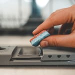 Käsi laittaa puolikkaan astianpesutabletin astianpesukoneen pesuainelokeroon – säästöniksi puolittamisesta