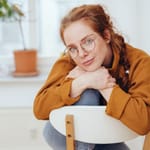 Rauhallinen introvertti nainen silmälaseissa nojaa tuoliin omissa ajatuksissaan — introversio on persoonallisuuden piirre, ei ujous