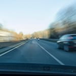 Vauhtisumeinen kuva henkilöauton tuulilasista nopeassa ohitustilanteessa moottoritiellä — auto ohittaa oikealla puolella