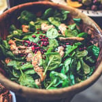 Puisessa kulhossa pinaattisalaatti grillattua kanaa ja granaattiomenaa, taustalla oliiveja ja muita ruokia.