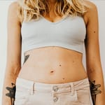 Blondi nainen seisoo vaaleassa crop topissa ja vaaleanpunaisissa farkuissa, tasainen vatsa näkyvissä