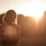Takaapäin vastavaloon otettu kuva, nainen istuu ulkona auringonlaskussa