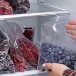 Käsi asettaa mustikkoja sisältävää pakastepussia täynnä olevaan pakastimeen, jossa on useita marjapusseja.
