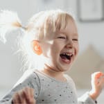 Iloinen vaaleatukkainen pikkulapsi nauraa ja juoksee valoisassa huoneessa