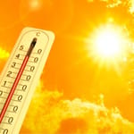 Valkoinen ulkolämpömittari, joka näyttää korkeita lukemia kuumasti loistavaa aurinkoa ja oranssinkeltaista taivasta vasten.