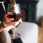 Nainen pitelee isoa punaviinilasia kädessään valoisassa olohuoneessa.