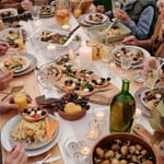 Runsas sukupäivällispöytä kynttilöineen ja ruokalajeineen, jonka ympärillä useat ihmiset ruokailevat yhdessä.