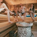 Uima-asu saunassa uimahalli: ihmisiä saunomassa lauteilla uima-asut päällä pyöreän kiukaan ympärillä.