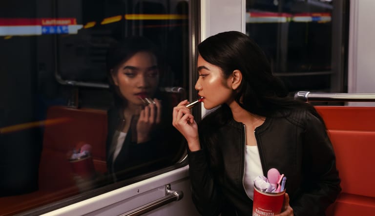 Nainen istuu metrossa ja meikkaa.