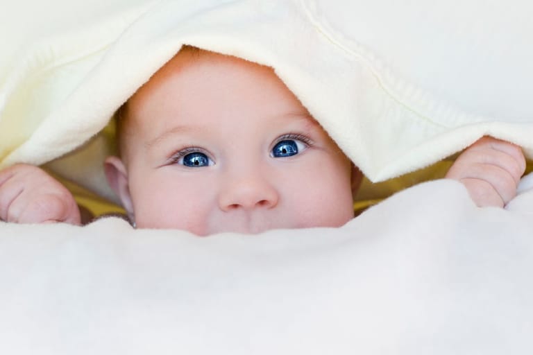 Vauva valkoisten peitteiden keskellä. Kuvituskuva.