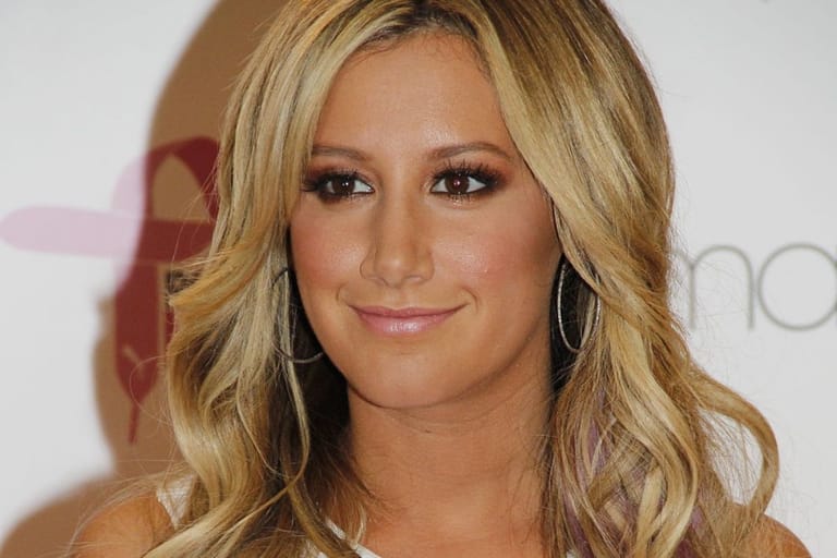 Näyttelijä Ashley Tisdale valkoista taustaa vasten punaisella matolla.