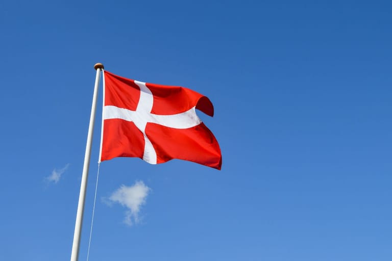 Tanskan lippu sinistä taivasta vasten hulmuaa tuulessa.
