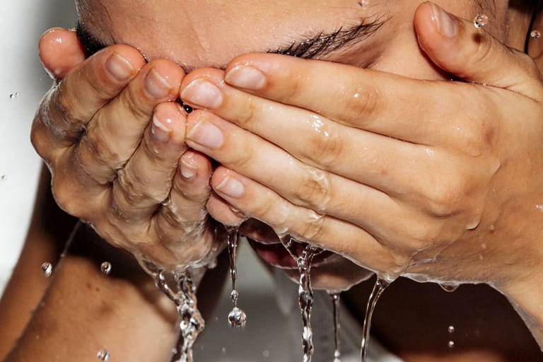 Henkilö pesee kasvojaan kylmällä vedellä, vesi valuu käsien välistä.