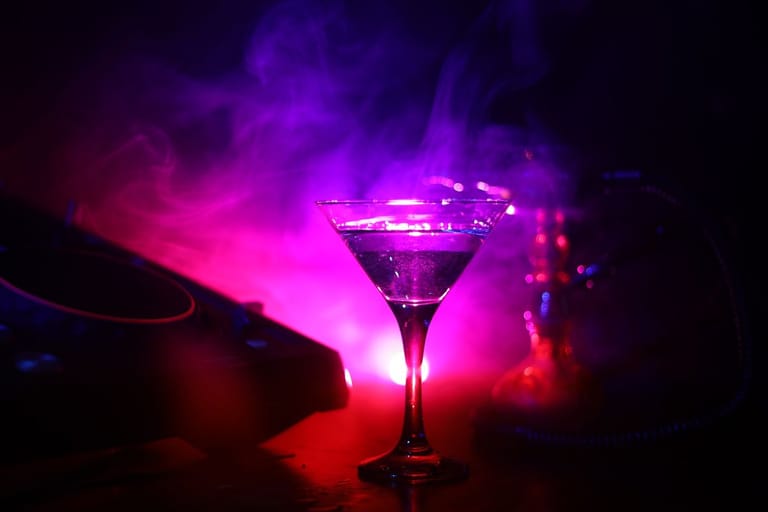 Cocktail-lasi DJ-pöydällä savun ja violetin valon ympäröimänä.
