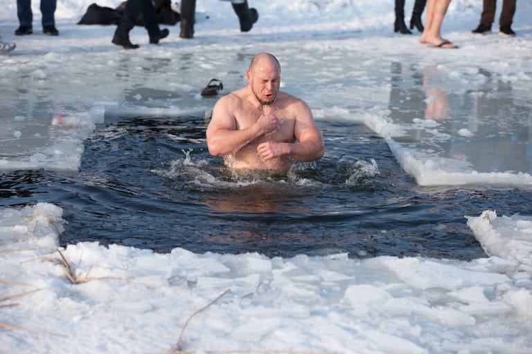 Henkilö nousee avannosta jäisessä vedessä muiden ihmisten seuratessa taustalla.