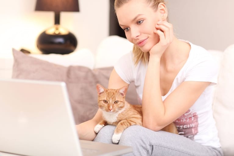 Nainen istuu tietokoneella kissa sylissä.