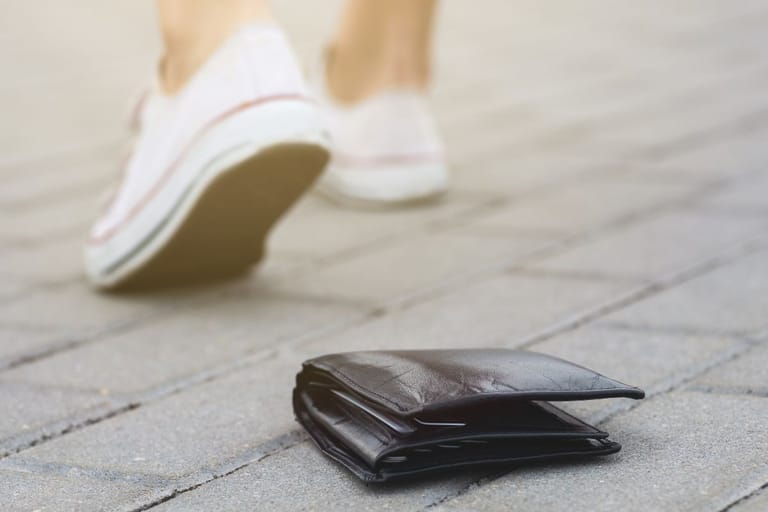 Miehen jalat valkoisissa tennareissa loittonevat maahan pudonneen nahkalompakon luota.