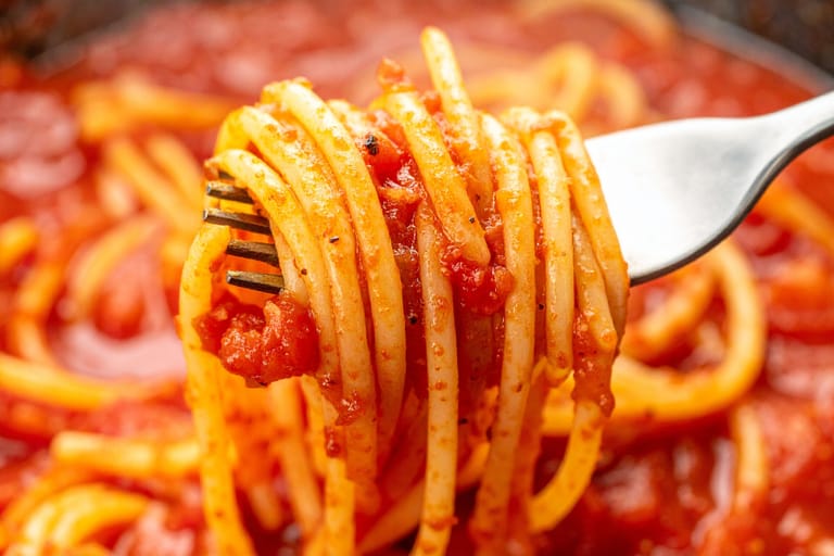 Haarukkaan kieputettu spagettia tomaattisessa kastikkeessa. Lähikuva.