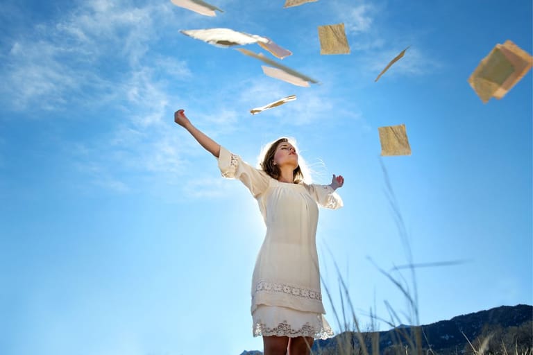 Nainen seisoo ulkona sinistä taivasta vasten ja heittää paperiarkkeja ilmaan, kädet levällään vapautuneessa asennossa. Naisen olemus symboloi irti päästämistä loputtomasta kontrolloinnista.