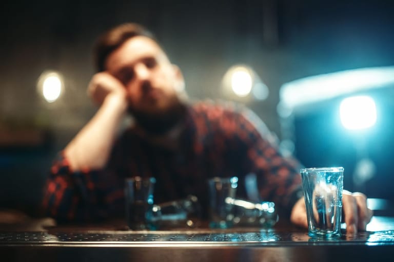 Baaritiskillä on muutama likainen shottilasi ja niiden takana epätarkkana miehen sieluetti, jolla on ruudullinen flanellipaita päällä ja jonka asento viittaa vahvaan humalatilaan.