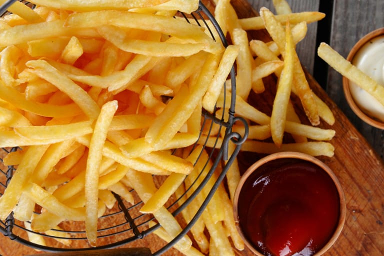 Kultaisia ranskalaisia perunoita tarjoiltuna ketsupin kanssa.