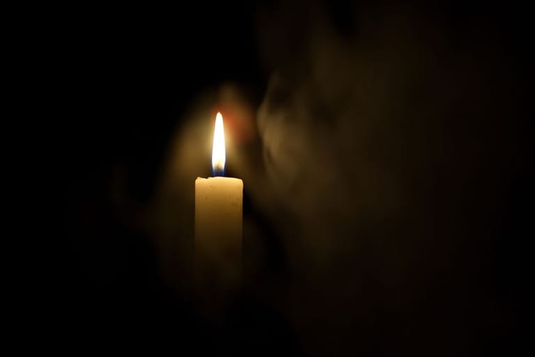 Pitkä kruunukynttilä palaa pimeässä.