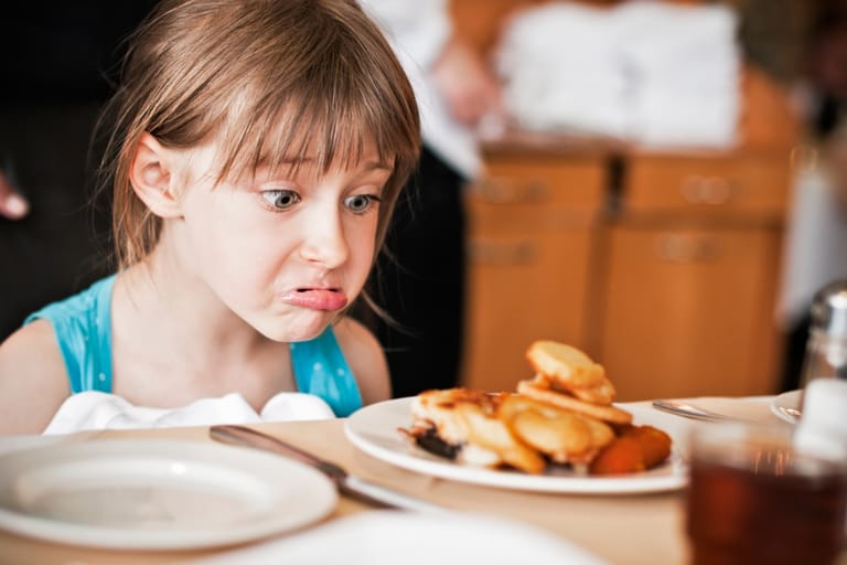 Lapsi katsoo epäilevästi lautasella olevaa ruokaa ruokapöydässä.