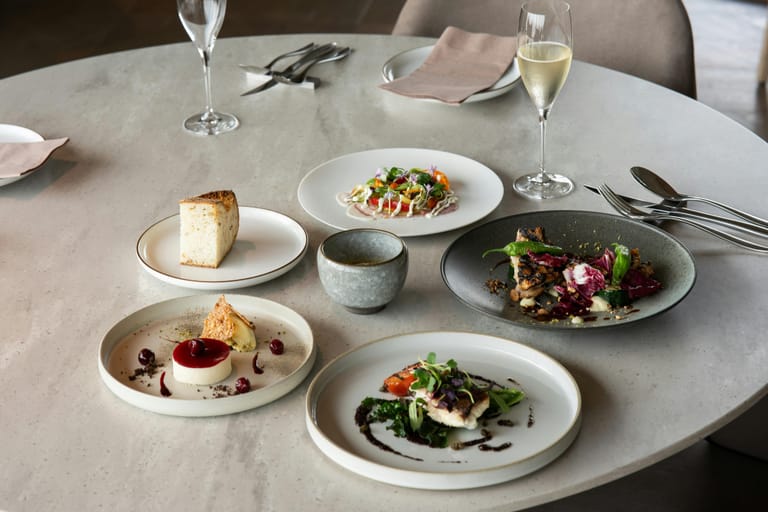 Useita ravintola-annoksia katettuna pöydälle viinilasien kanssa.