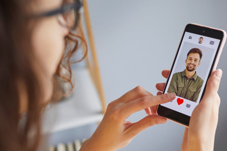 Henkilö selaa deittisovellusta puhelimellaan ja painaa sydän-ikonia miehen profiilikuvan kohdalla.