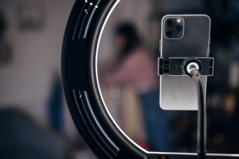 Älypuhelin kiinnitettynä jalustaan rengasvalon keskellä, taustalla epätarkka sisätila.