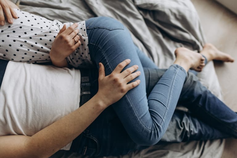 Kaksi aikuista makaa sängyssä kyljellään, toisen käsi lepää toisen reidellä