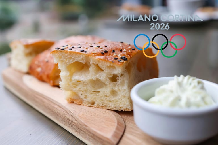 Laudalla pala focaccia-leipää. Vieressä tuorejuustoa kupissa ja kuvan päällä olympialaisten logo.