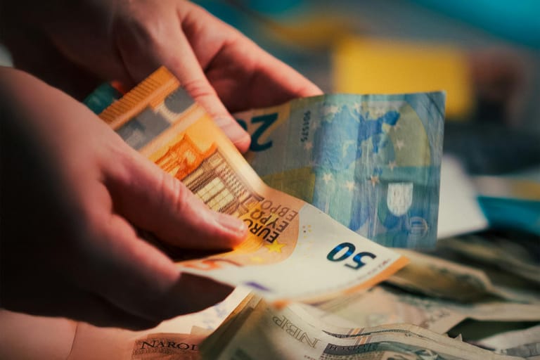 Lähikuva käsistä, jotka laskevat 50 ja 20 euron seteleitä pöydän yllä muiden setelien päällä.