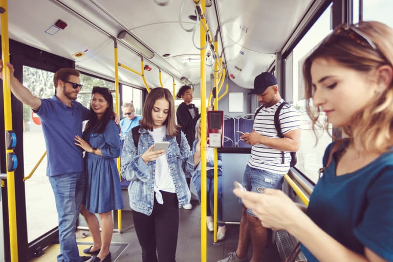 Matkustajat seisovat bussissa ja selaavat älypuhelimiaan, kukaan ei ole katsekontaktissa toistensa kanssa.