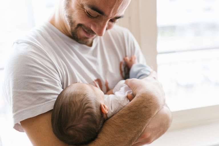 Isä pitää vastasyntynyttä vauvaa sylissään ja katsoo sitä hymyillen.