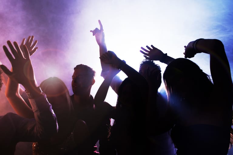 Ihmiset tanssivat ja nostavat käsiään ilmassa värikkäissä juhlavaloissa.