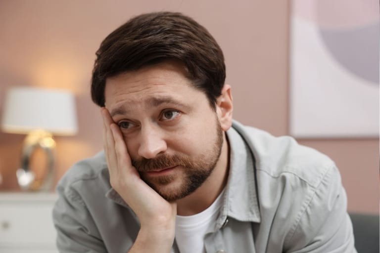 Mies nojaa käteensä ja katsoo hieman väsyneenä sivulle sisätiloissa.