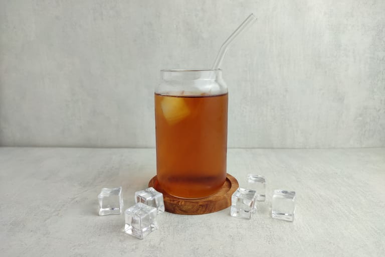 Lasipurkissa tarjoiltu jäätee jääpaloilla ja lasipillillä, pöydällä muutama irrallinen jääpala.