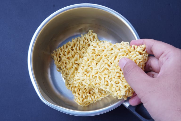 Käsi laittaa kuivat pikanuudelit kattilaan ennen keittämistä.