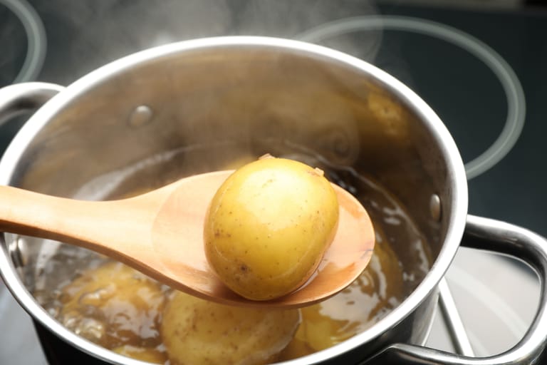 Puulusikalla nostettu keitetty peruna höyryävästä kattilasta liedellä.