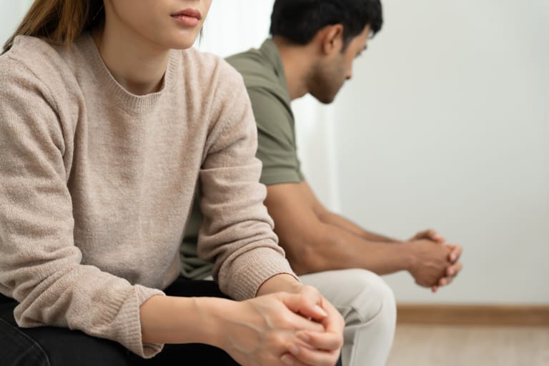 Nainen ja mies istuvat erillään vakavina, jännittynyt tunnelma parisuhteessa.