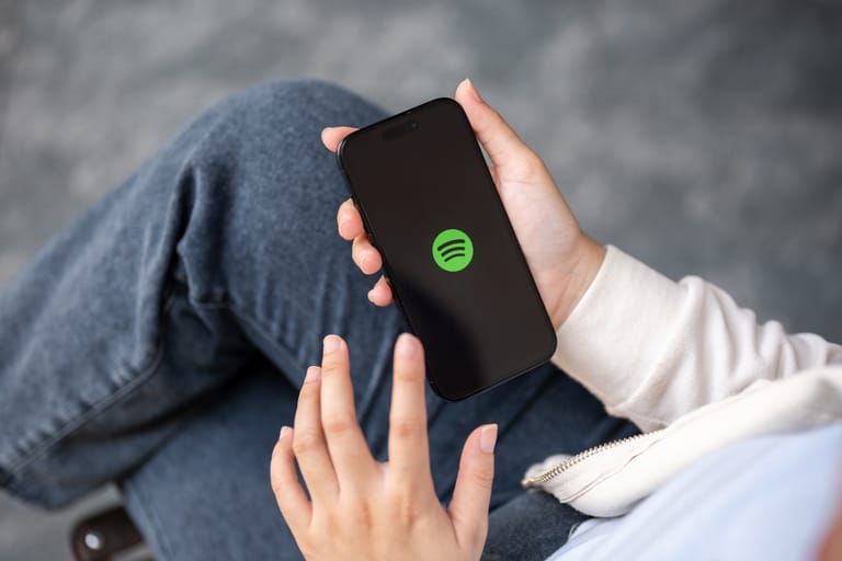 Henkilö pitää kädessään älypuhelinta, jonka näytöllä näkyy Spotify-sovelluksen logo.