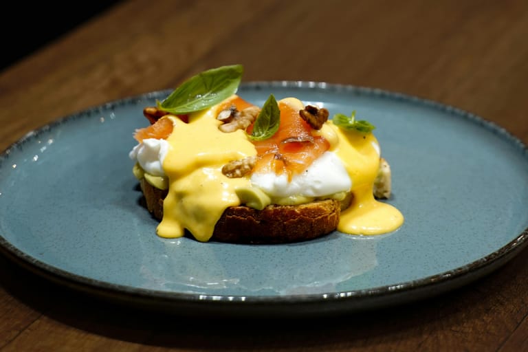 Annos lautasella: paahdetun leivän päällä avokadoa, uppomuna, savulohta ja hollandaise-kastiketta, koristeltu yrteillä ja pähkinöillä.