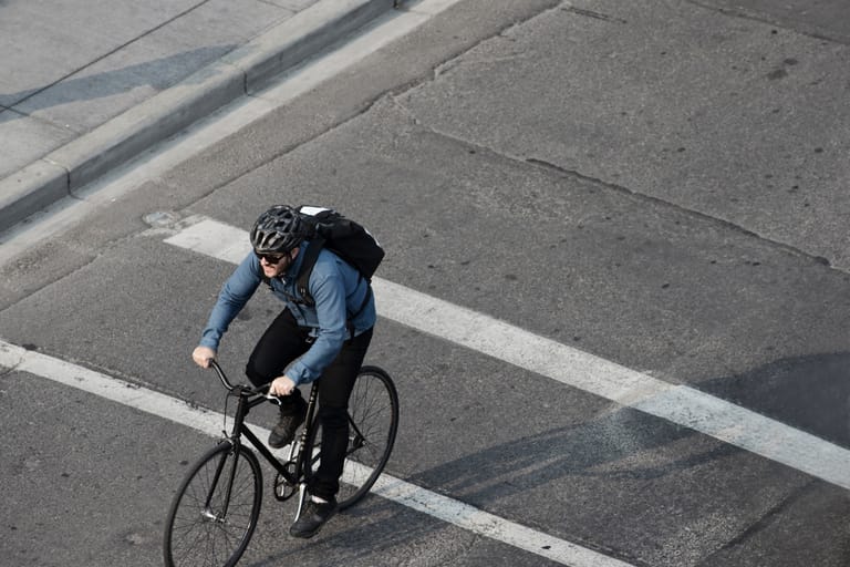 Kypärää käyttävä pyöräilijä ylittää katua kaupungissa.