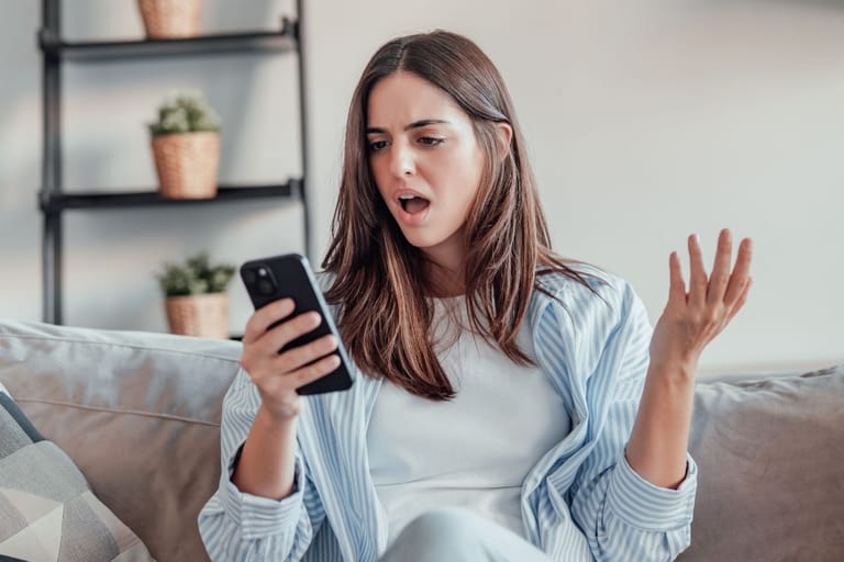 nainen turhautuneena selaa deittisovellusta puhelimella kotona