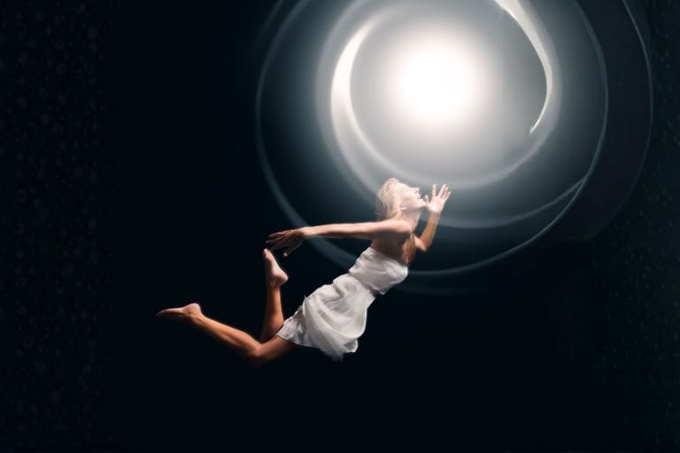 Nainen leijumassa kohti kirkasta valoa symboloimassa tietoisuuden jatkumista ja kvanttikuolemattomuutta