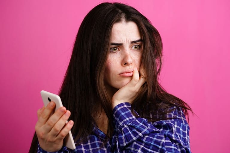 nainen katsoo puhelinta huolestuneena eikä vastaa viestiin heti