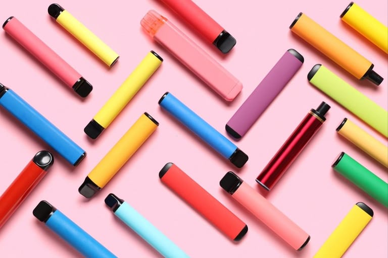 Värikkäitä kertakäyttöisiä vape-laitteita levitettynä pöydälle – nuorten suosima sähkösavuketrendi