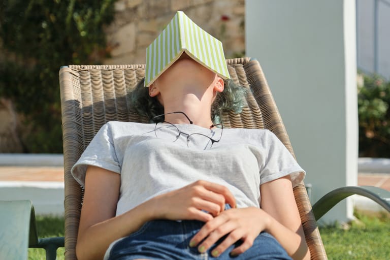 Nuori makaa tuolissa kirja naaman päällä.